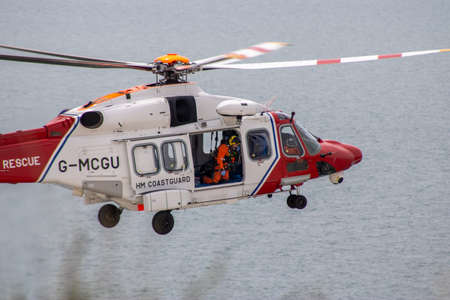 East Sussex, Beachy Head, UK 10th July 2019: The HM Coastguard Rescue Helicopter attending an incident on the Beachy Head cliffs flying in the sky on a bright cloudy day over the ocean.のeditorial素材