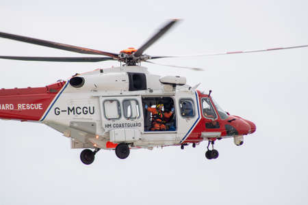 East Sussex, Beachy Head, UK 10th July 2019: The HM Coastguard Rescue Helicopter attending an incident on the Beachy Head cliffs flying in the sky on a bright cloudy day over the ocean.のeditorial素材