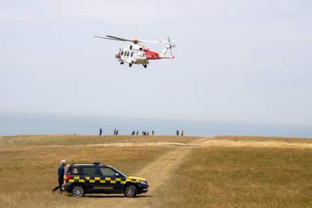East Sussex, Beachy Head, UK 10th July 2019: The HM Coastguard Rescue Helicopter attending an incident on the Beachy Head cliffs flying in the sky on a bright cloudy day over the ocean.のeditorial素材