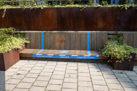 Leeds UK, 12th Aug 2020: A bench in the area of Leeds known as The Leeds Dock, the bench has stickers on it reminding people to sit 2 metres apart and says 1 Person or 1 couple onlyのeditorial素材
