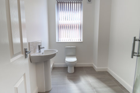 Photo of a modern brand new British bathroom showing a newly installed Toilet and Basin sink, with tiled grey floor, white walls and skirting boards with blinds up at the windowの写真素材