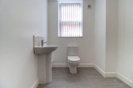 Photo of a modern brand new British bathroom showing a newly installed Toilet and Basin sink, with tiled grey floor, white walls and skirting boards with blinds up at the windowの写真素材