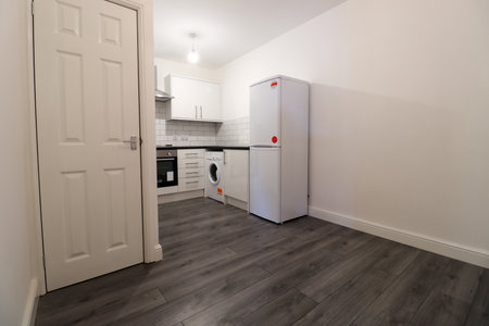 A modern British apartment kitchen with a grey wooden floor with white walls and modern fitted kitchen with washing machine, cooker stove and white fridge.の写真素材