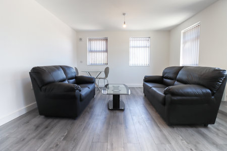 A modern British living room with two black leather sofas and a dining table on a grey wooden floor with white walls and modern blinds up at the windowの写真素材