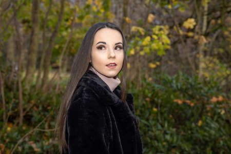 A young attractive woman with long brown hair in the winter time in a woodland park wearing a black coatの写真素材