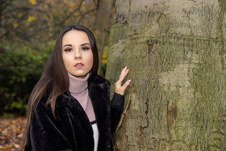 A young attractive woman with long brown hair in the winter time in a woodland park wearing a black coatの写真素材
