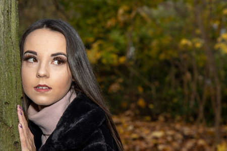A young attractive woman with long brown hair in the winter time in a woodland park wearing a black coatの写真素材