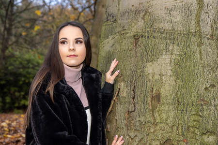 A young attractive woman with long brown hair in the winter time in a woodland park wearing a black coatの写真素材