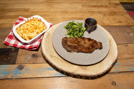 A delicious tender tenderloin steak on a plate with a a pot of red wine sauce and garnish on a wooden kitchen tableの写真素材