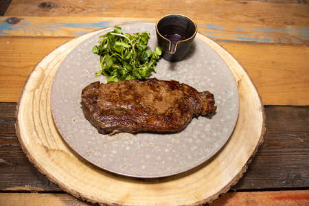 A delicious tender tenderloin steak on a plate with a a pot of red wine sauce and garnish on a wooden kitchen tableの写真素材