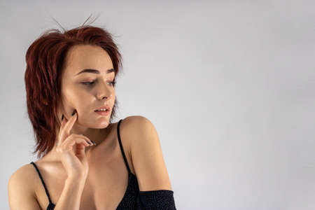 A young female attractive caucasian model with album red hair in a studio with a white background wearing a black dress.の写真素材