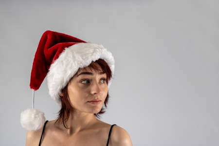 Young female attractive model with auburn hair and red lipstick in a studio with a white background wearing a sexy santa Santa hat with a black going out dressの写真素材