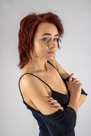 A young female attractive caucasian model with album red hair in a studio with a white background wearing a black dress.の写真素材