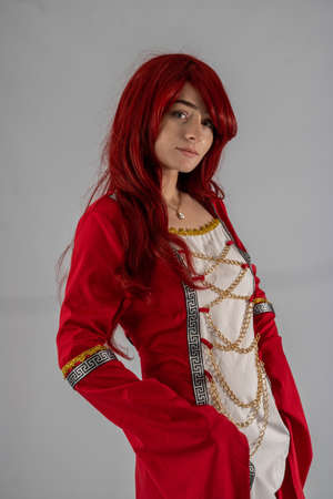 Full length young female attractive model in a studio with a white background, the model is wearing a red medieval costume with red auburn hairの写真素材