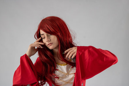 Full length young female attractive model in a studio with a white background, the model is wearing a red medieval costume with red auburn hairの写真素材