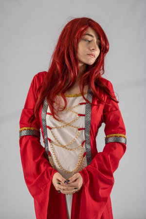 Full length young female attractive model in a studio with a white background, the model is wearing a red medieval costume with red auburn hairの写真素材