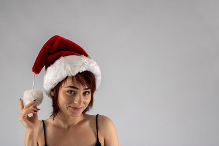 Young female attractive model with auburn hair and red lipstick in a studio with a white background wearing a   santa Santa hat with a black going out dressの写真素材