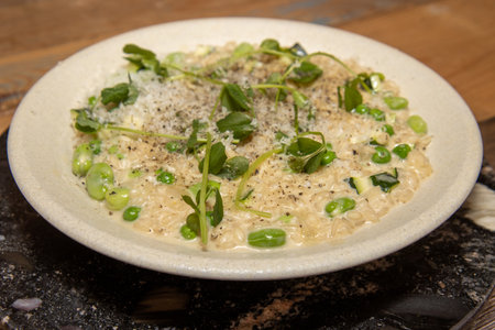 A delicious meal of courgette, broad bean and pea risotto, on a wooden kitchen tableの写真素材
