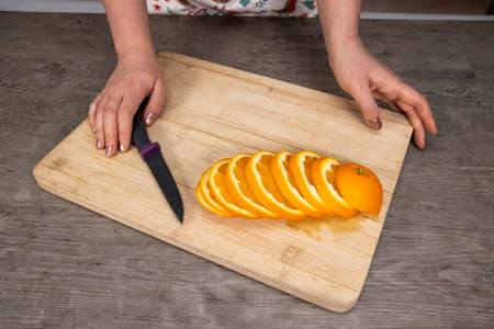 A woman in a kitchen cutting an orange on a wooden chopping board fruit salad healthy eating conceptの写真素材