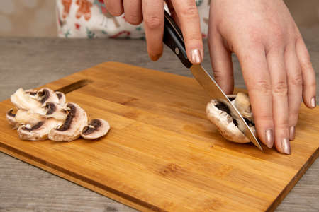 A woman in a kitchen cutting up a mushroom on a wooden chopping board, home cooking conceptの写真素材