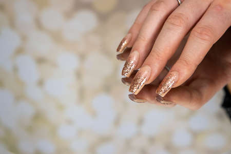 A woman's hand with gold glittery nails on a mirror backgroundの写真素材