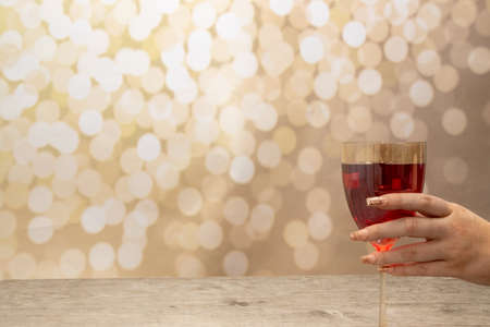 A woman's hand with long elegant nails holding a glass of rose wine on a glittery gold backgroundの写真素材