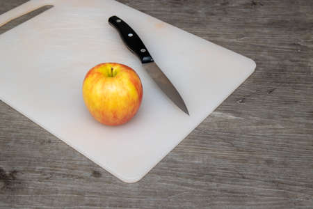 A plastic chopping board in a kitchen with a knife next to an appleの写真素材