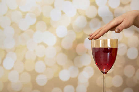 A woman's hand with long elegant nails holding a glass of rose wine on a glittery gold backgroundの写真素材
