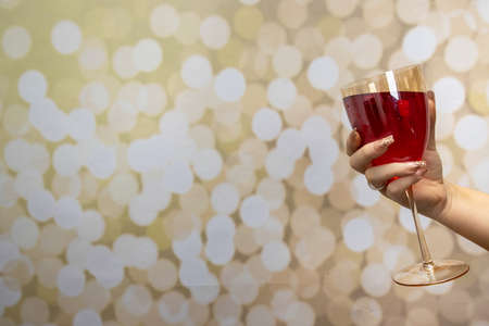 A woman's hand with long elegant nails holding a glass of rose wine on a glittery gold backgroundの写真素材