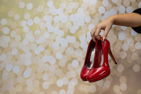 A woman's hand with gold glittery nails holding a pair or red shoes on a glittery backgroundの写真素材