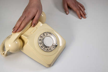 An old retro telephone on a white background being answered by an elegant womanの写真素材