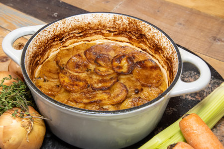 A classic British hot pot stew with slices of potatoes on top, surrounded by the ingredients used to cook the traditional winter dishの写真素材