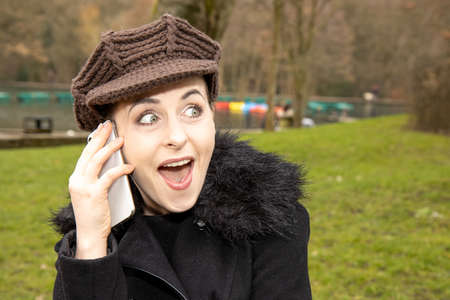 An attractive young woman in a public park on a cold day in the winter time on the phone looking...
