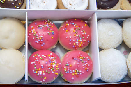 A delicious box selection of colourful doughnuts, including pink and chocolate ones with sprinkles