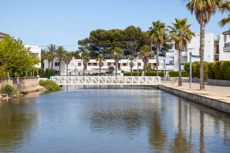The beautiful beach front on the Island of Majorca in Spain showing a bridge going over water by holiday homes on a hot sunny summers dayの写真素材