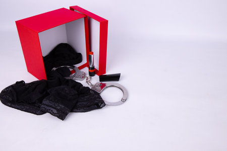 A red gift box filled with sexy romantic items and lingerie inside like stockings, hand cuffs and sexy red lipstick, romance valentines gift box conceptの写真素材