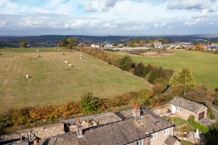 Aerial drone photo of the town of Huddersfield in West Yorkshire, England showing old cottages and a farmers field with animals grazing in the field taken in the autumn time.の写真素材