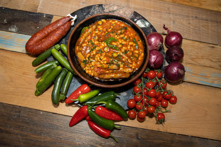 A bowl of delicious beans and sausages topped with garnish surrounded by the ingredients used to make the dishの写真素材