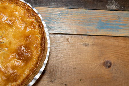 A delicious cooked meat pie showing the tasty meat pie and crust topping on a wooden kitchen table or work topの写真素材