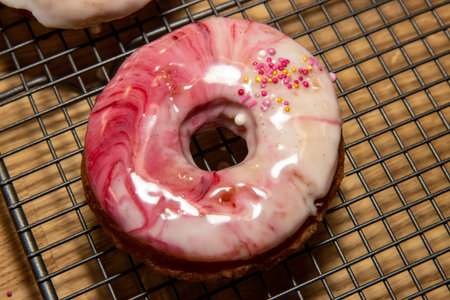 A selection of oil fried doughnuts topped with sweet pink and white icing and sprinkles on a baking treyの写真素材