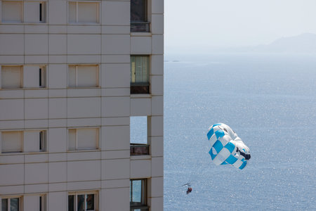 Photo of a Parasailer who is Parasailing over the ocean in the city of Benidorm in Spain next to an apartment blockの写真素材