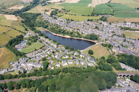 Aerial photo of the historic Yorkshire town of Huddersfield in the UK, showing the residential housing estates by a lake and train viaduct on a sunny day in the summer timeの写真素材