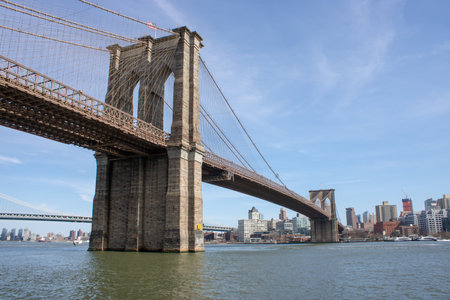 The famous Brooklyn Bridge Bridge located in New York City in the United States of America showing the east river and Brooklyn Heights in the background taken on a beautiful sunny part cloudy dayの写真素材