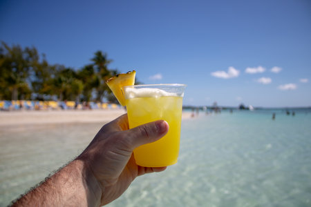 Close up of a yellow and orange tropical cocktail drink being held by a hand on a beautiful tropical beach.の写真素材