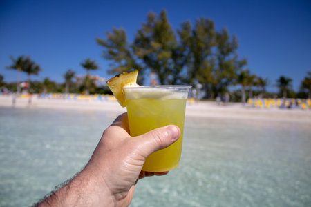 Close up of a yellow and orange tropical cocktail drink being held by a hand on a beautiful tropical...