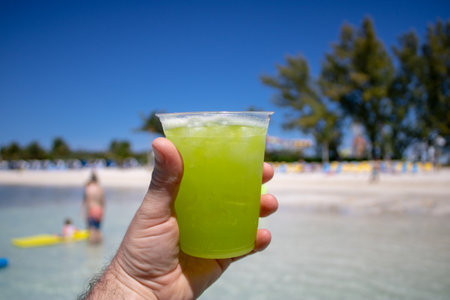 Close up of a tropical cocktail drink being held by a males hand on a beautiful tropical beach.