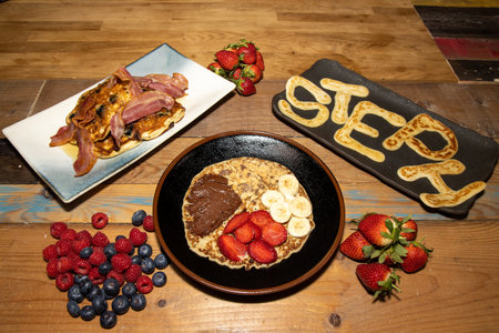 A delicious pancake with strawberries, bananas and chocolate spread on a wooden kitchen table with toast and bacon and a pancake spelling out the name Stephの写真素材