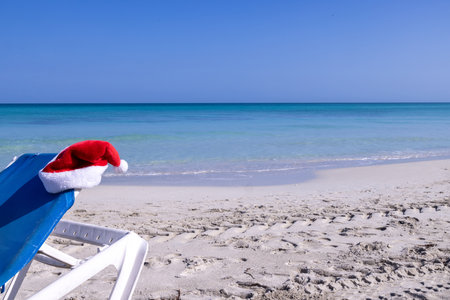 A red Christmas Santa Clause hat on blue and white sun lounger on the beach taken on a beach in the town of Varadero in Cuba, Christmas holidays in the sun and on the beach conceptの写真素材