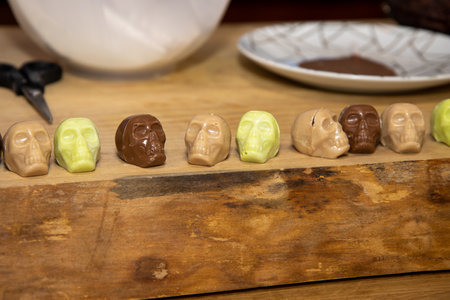 A row of delicious chocolates in the shape of a skull or skeleton placed on a wooden table for halloweenの写真素材