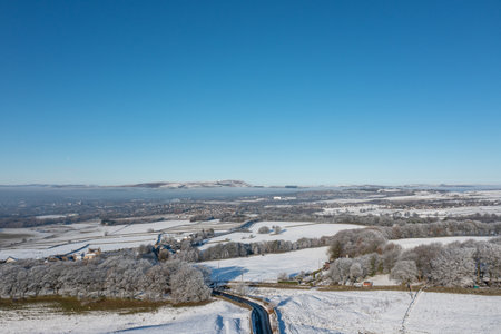 Aerial drone photo of the town of Mereclough in the town of Burnley in Lancashire, England showing the farmers fields on a snowy winters day in the UK with snow covering the fields and a blue sky.の写真素材